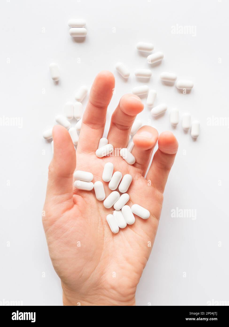 Palm hand full of white scattering pills. Capsules with medicines on light background. Flat lay, top view. Stock Photo