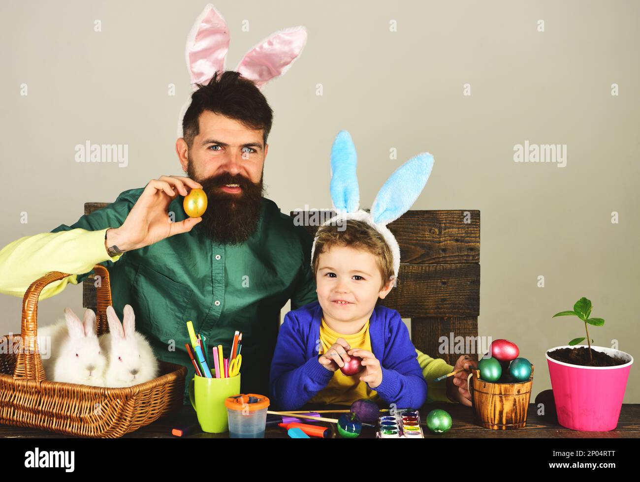 Happy family father and son painting eggs for Easter holiday. Cute child boy and bearded man in rabbit ears with painted eggs on Easter day. Dad and Stock Photo