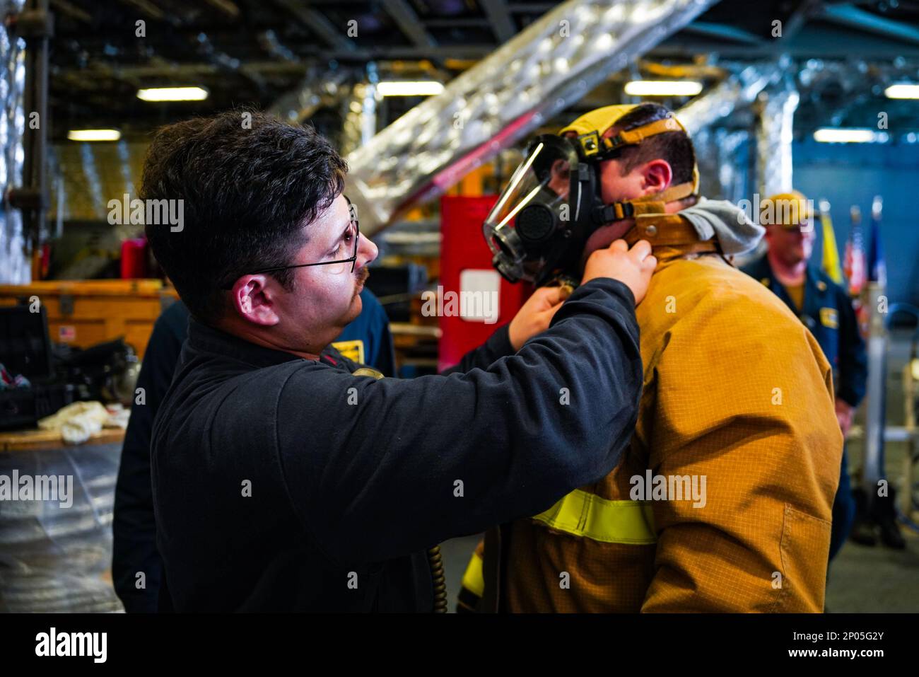 SINGAPORE (Jan. 21, 2023) Electrician’s Mate 1st Class Christopher Rivera, left, from Bayamon, Puerto Rico, assists Sonar Technician (Surface) 3rd Class Bryan Blasing, from Seattle, as he dons personal protective equipment during a damage control drill aboard Independence-class littoral combat ship USS Oakland (LCS 24) at Changi Naval Base, Singapore, Jan. 21, 2023. Oakland, part of Destroyer Squadron 7, is on a rotational deployment operating in the U.S. 7th Fleet area of operation to enhance interoperability with partners and serve as a ready-response force in support of a free and open Indo Stock Photo