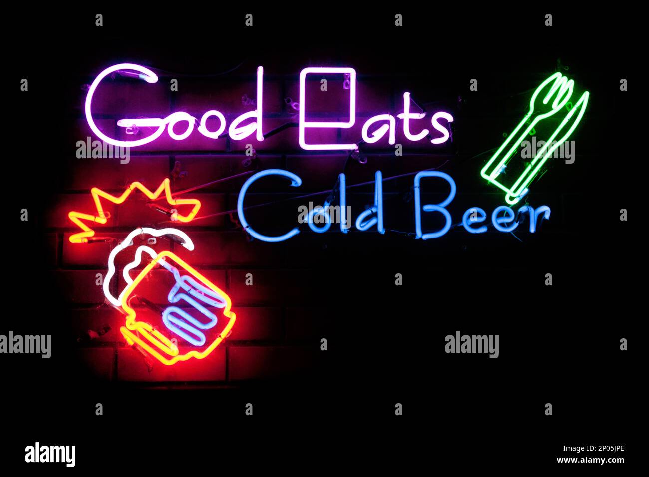 Neon light shaped into the phrase “Good Eats Cold Beer” with on its left a knife and fork and on its bottom left a pint of beer. Stock Photo
