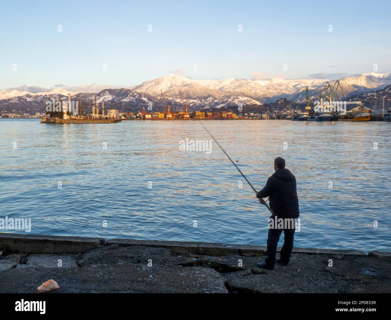 Catcher on spinning in the port area against the backdrop of the mountains.  Fishing in Batumi. Lure fishing. Silhouette of a fisherman. Spinning. Spor  Stock Photo - Alamy