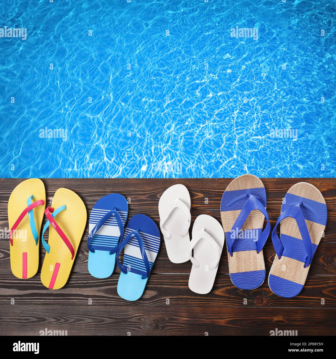 Pairs of flip flops on wooden deck near swimming pool, flat lay Stock ...