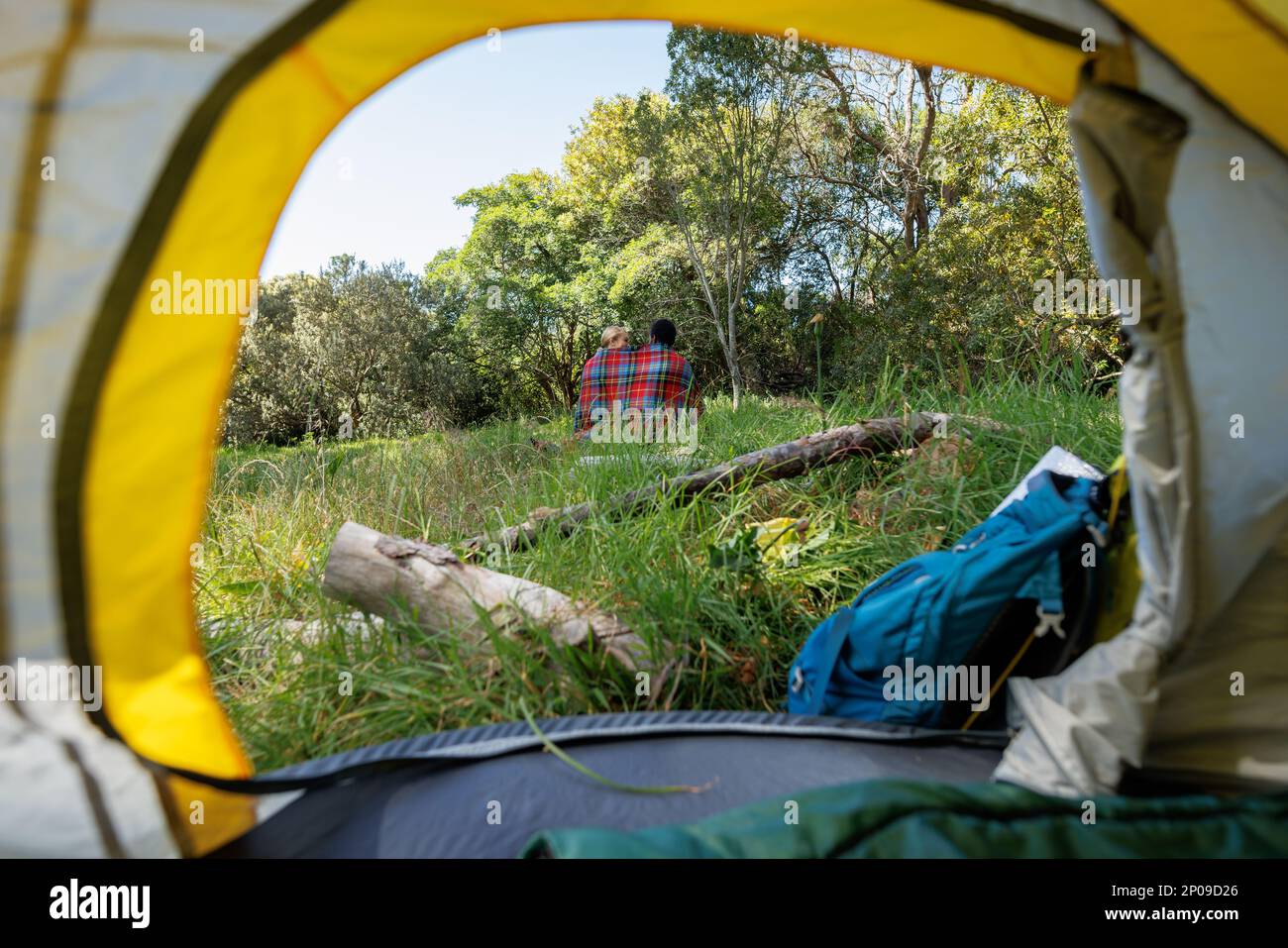 Rear view from in tent of diverse couple camping, sitting with blanket