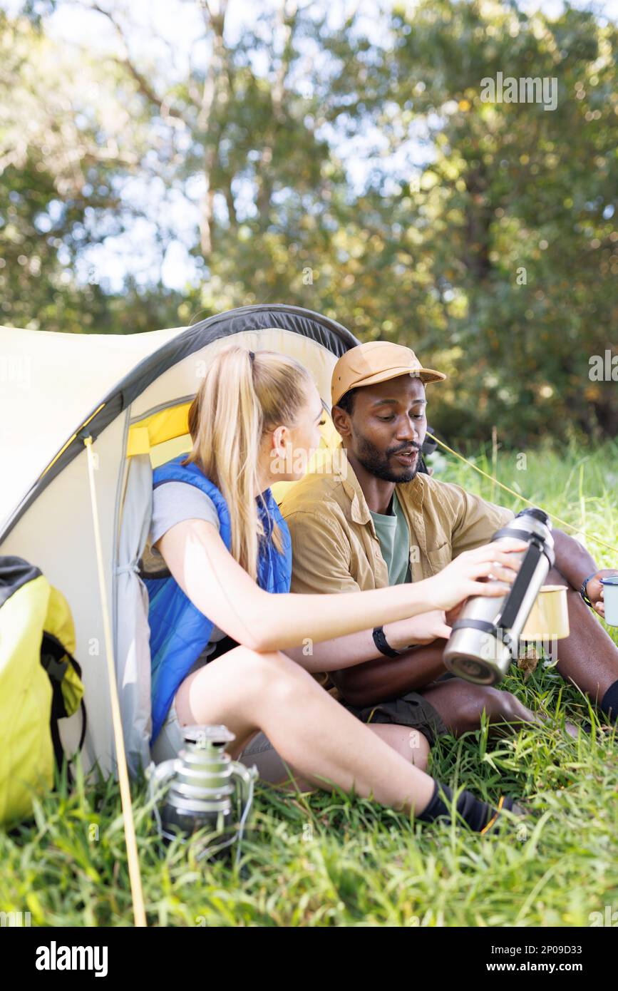 Vertical of happy, diverse couple in forest sitting in front of tent ...