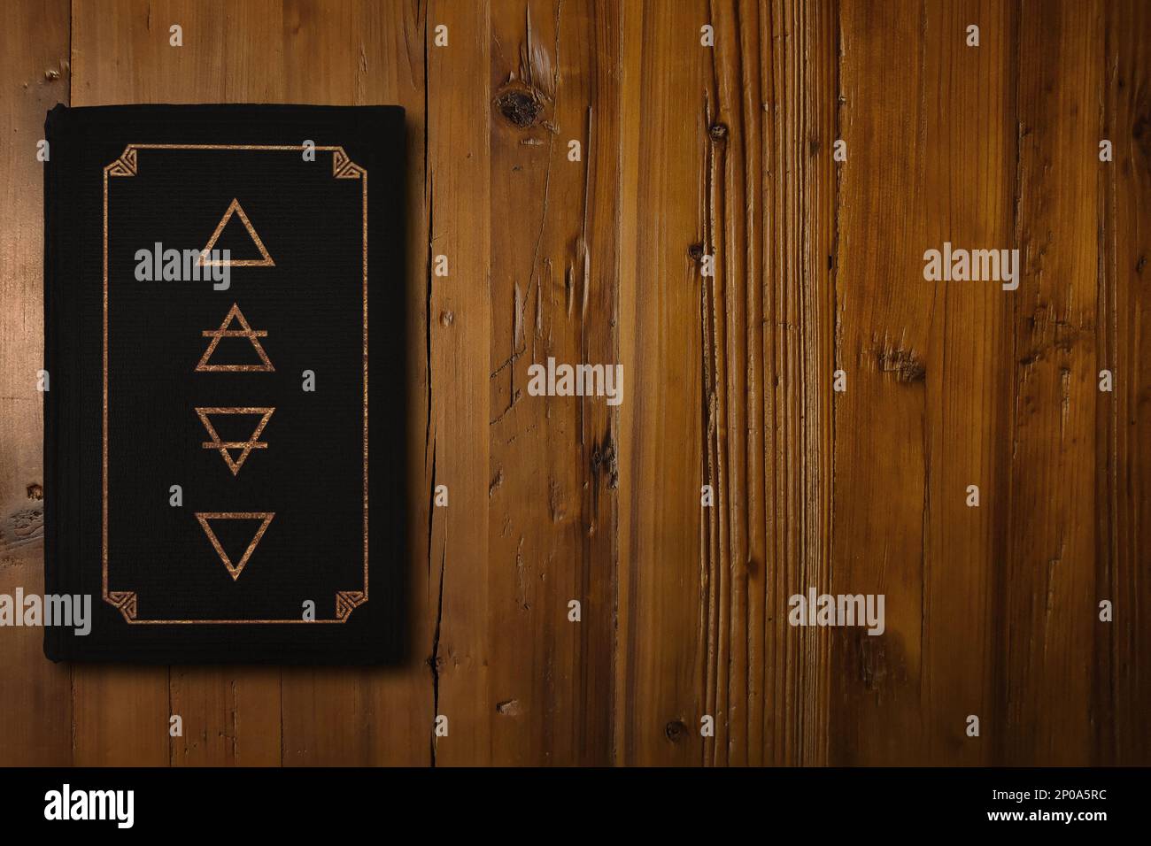 Close-up on black Alchemy book with a gilded Four Elements (Fire, Air, Earth and Water) in its middle. Stock Photo