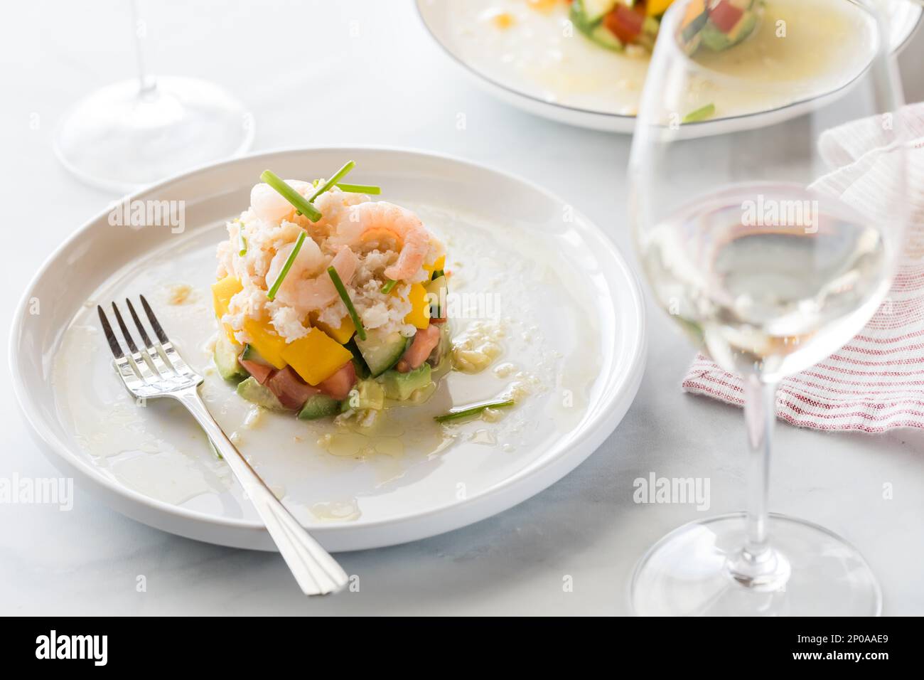 A crab stack salad served with white wine and light coming from behind ...