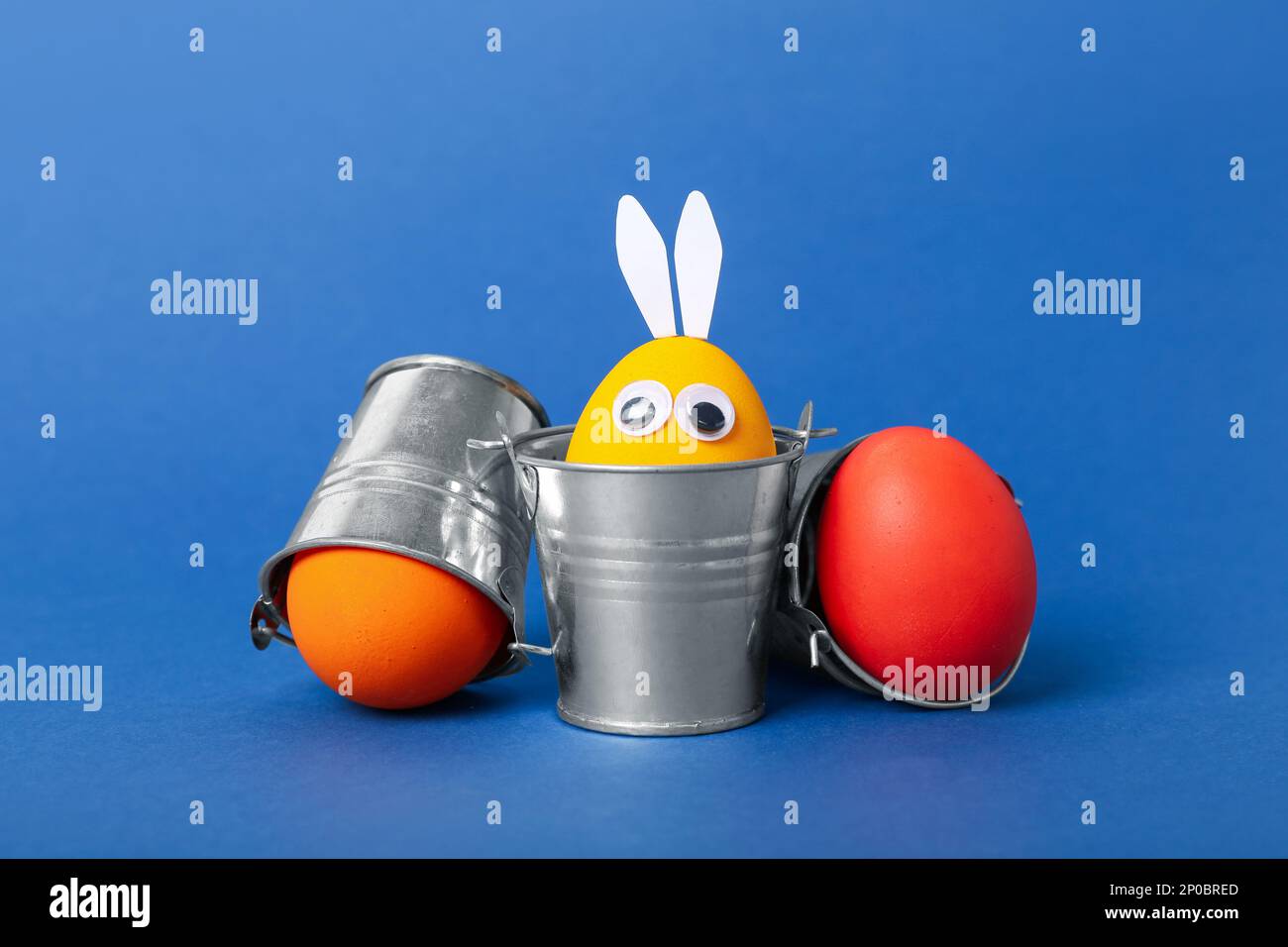 Funny Easter eggs in buckets on blue background Stock Photo