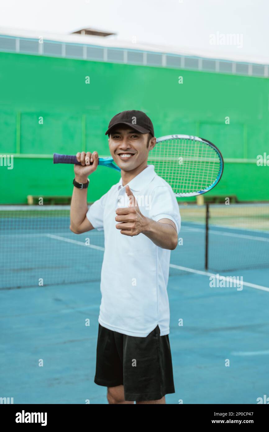 smiling male athlete with thumbs up while carrying racket Stock Photo ...