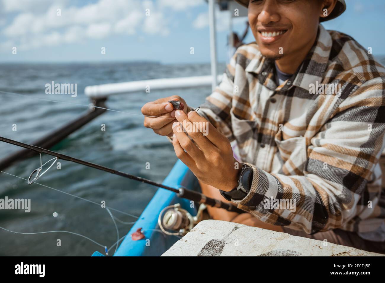 Asian angler puts bait on a hook while fishing on a small fishing boat ...
