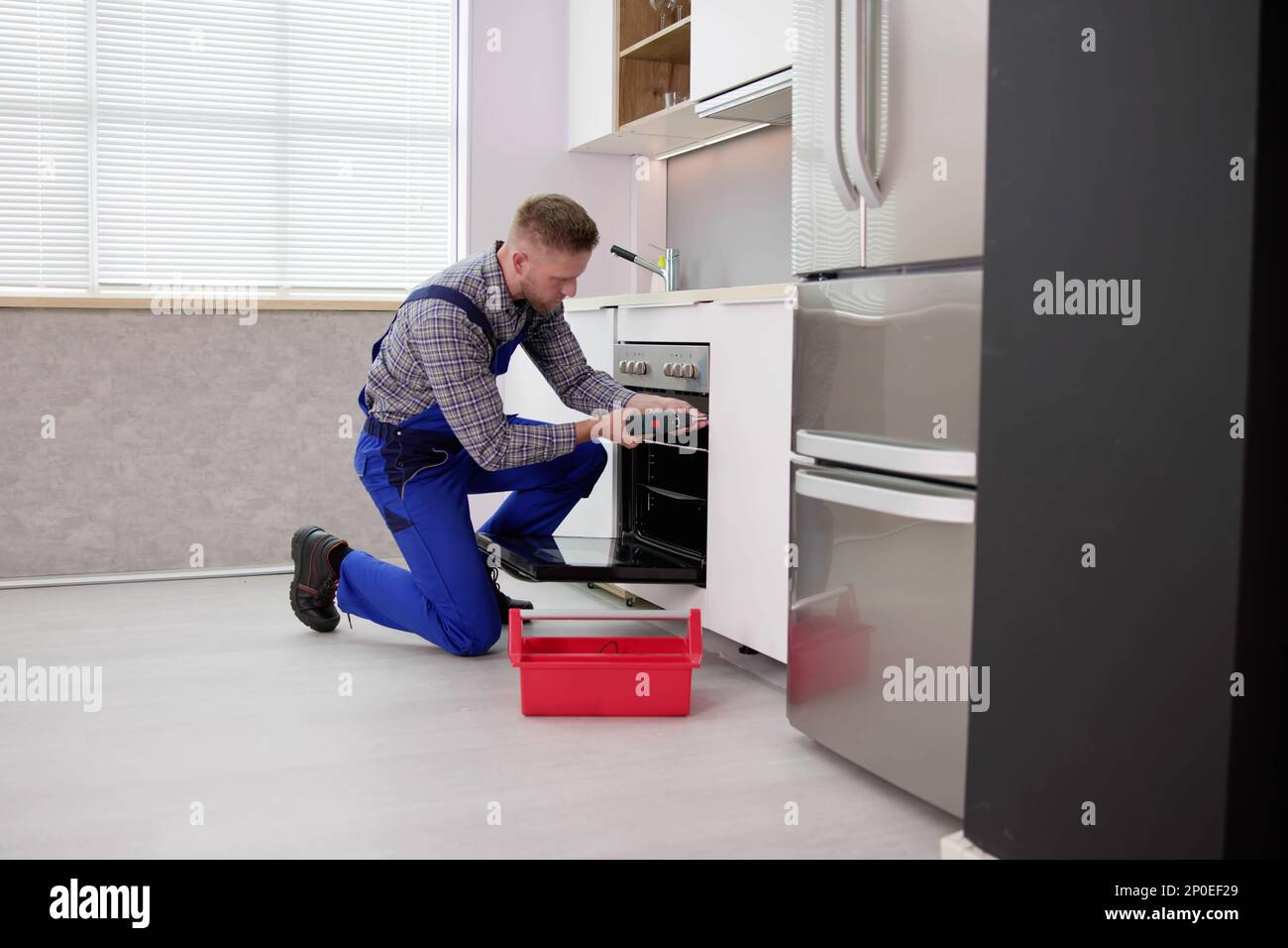 Young Man In Overall Repairing Washing Machine Stock Photo