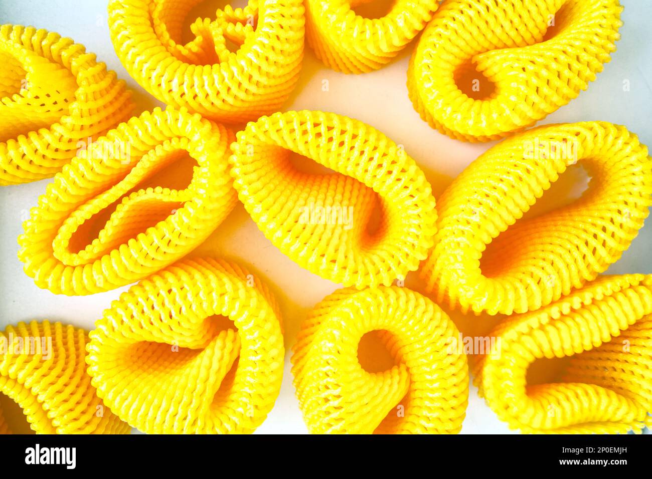 Many yellow EPE fruit nets abstract close-up background. Expanded polyethylene foam net pile Stock Photo