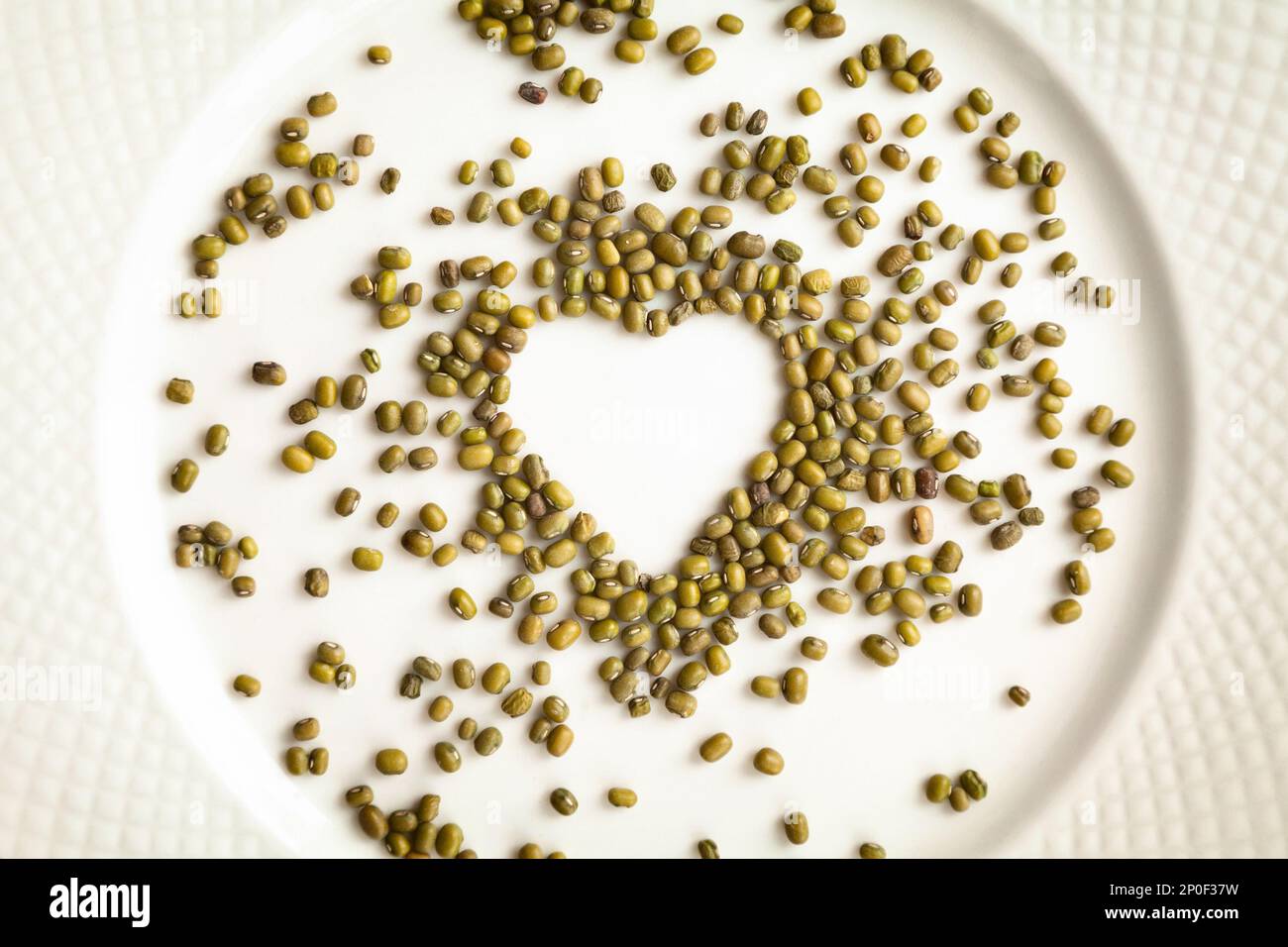 Mung beans in a shape of heart isolated on a white plate. Raw green gram groats food ingredient background. Love for cooking concept Stock Photo