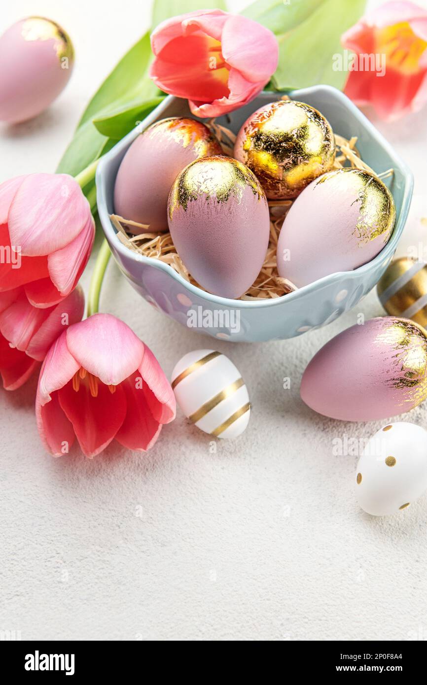 Bowl with Easter eggs painted gold and pastel colors and pink tulips on ...