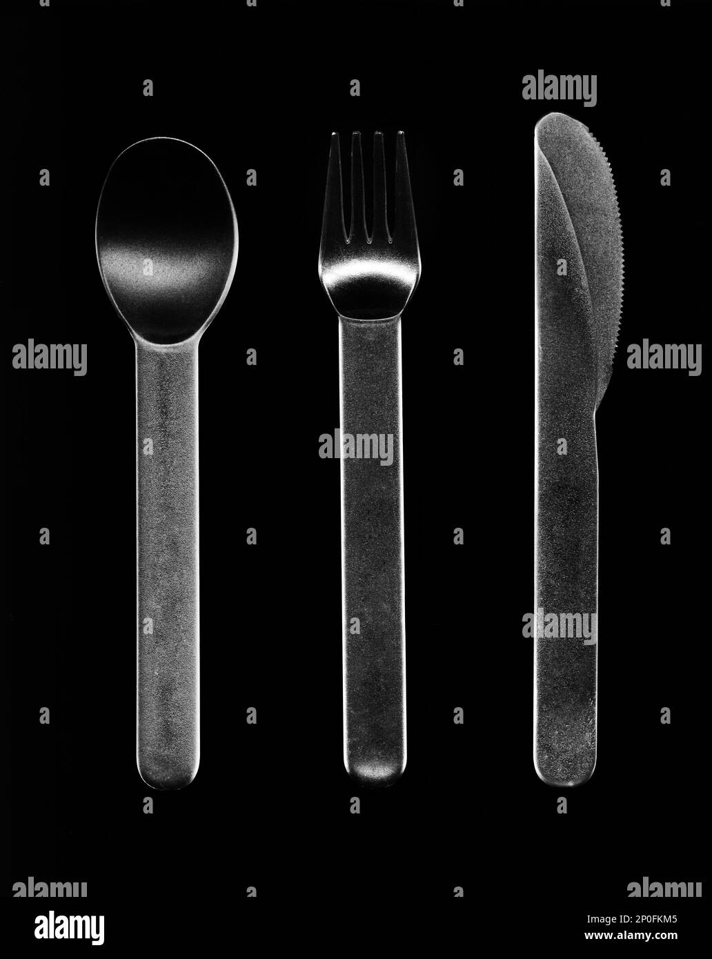 Cheap plastic cutlery set isolated on black. Disposable clear silverware -  knife, spoon and fork arranged in a row. Eating utensils Stock Photo