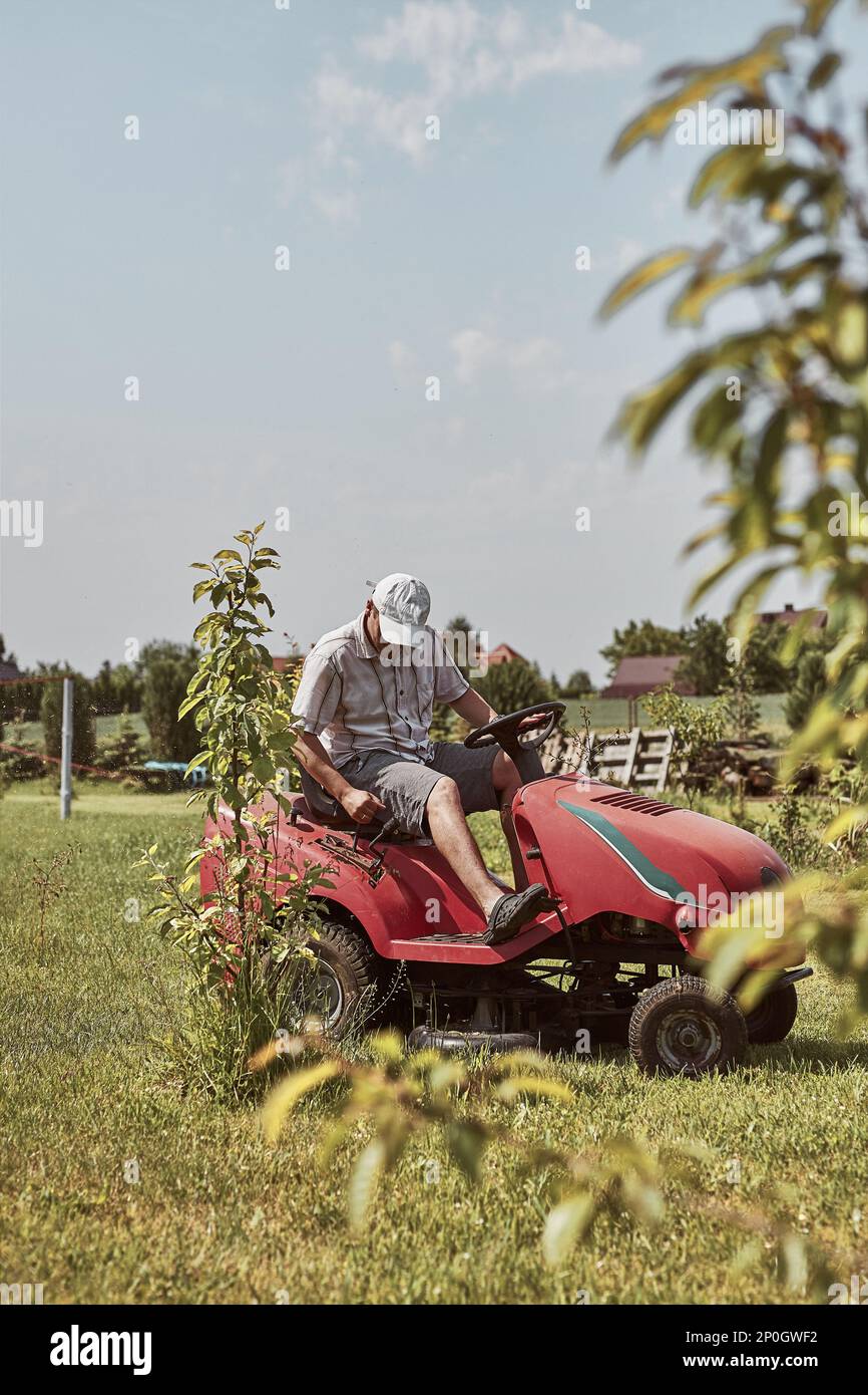 Man mowing his lawn using riding lawnmower. Man maintaining grass in his garden beside house Stock Photo