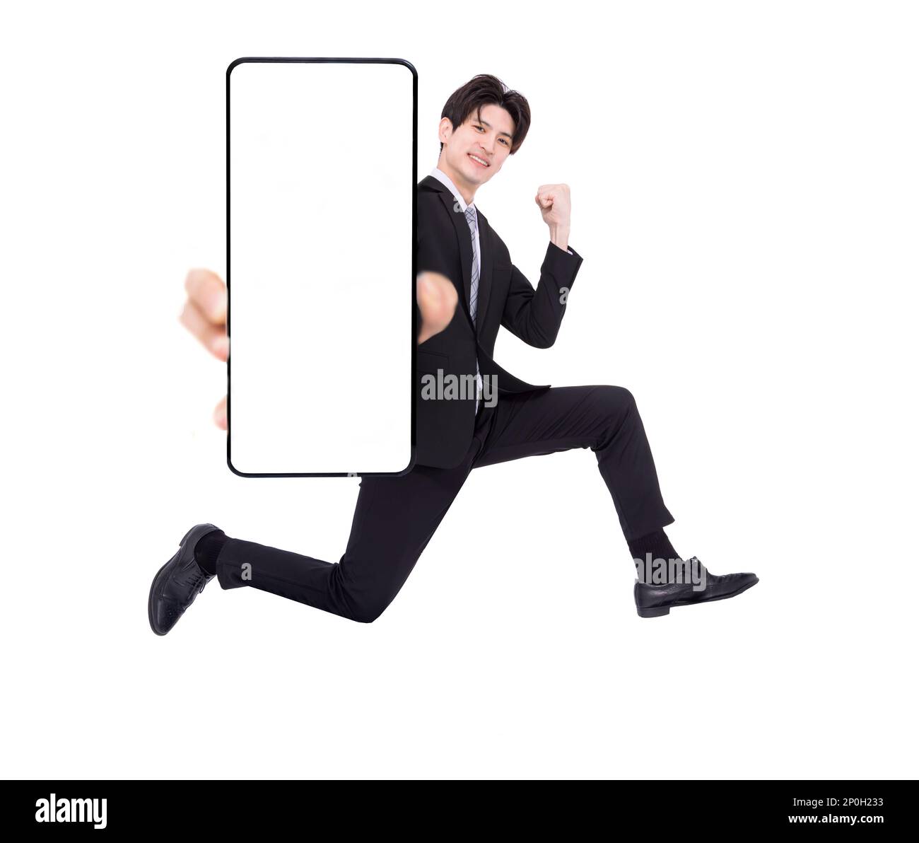 Happy young business man jumping and showing blank mobile phone screen