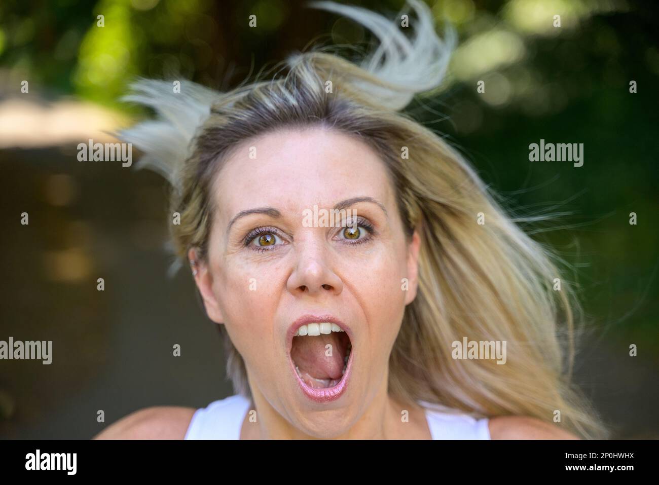 Angry middle aged woman yelling at the camera in frustration outdoors in a garden Stock Photo