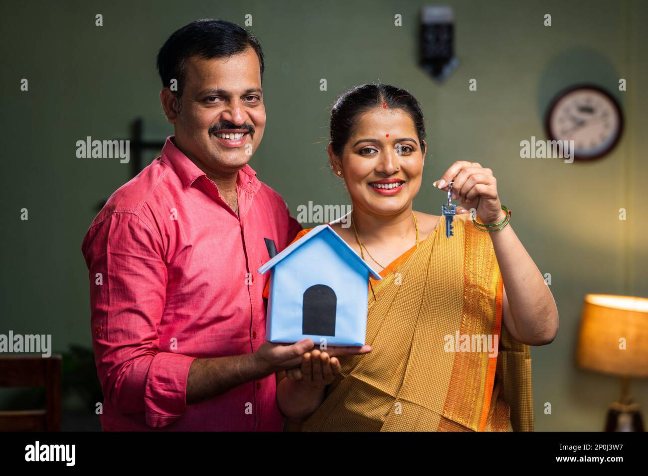 Happy smiling couple showing new house keys by toy home while looking camera - concept of new home purchasing, home loan and investment. Stock Photo