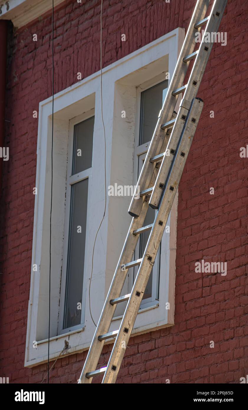 An extension ladder leans against the front of a multifamily housing building in preparation of roof repairs. Stock Photo