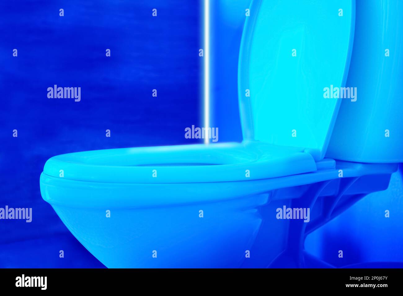Toilet bowl in public restroom lit with UV blue light, closeup view