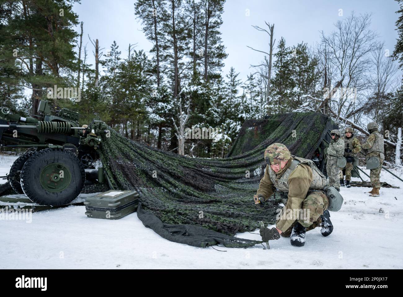 Army Pfc. Cameron Patzner, 1-120th Field Artillery Regiment, hammers in a stake to help secure a camouflage canopy while setting up an M119 howitzer during Northern Strike 23-1, Jan. 25, 2023, at Camp Grayling, Mich. Units that participate in Northern Strike’s winter iteration build readiness by conducting joint, cold-weather training designed to meet objectives of the Department of Defense’s Arctic Strategy. Stock Photo