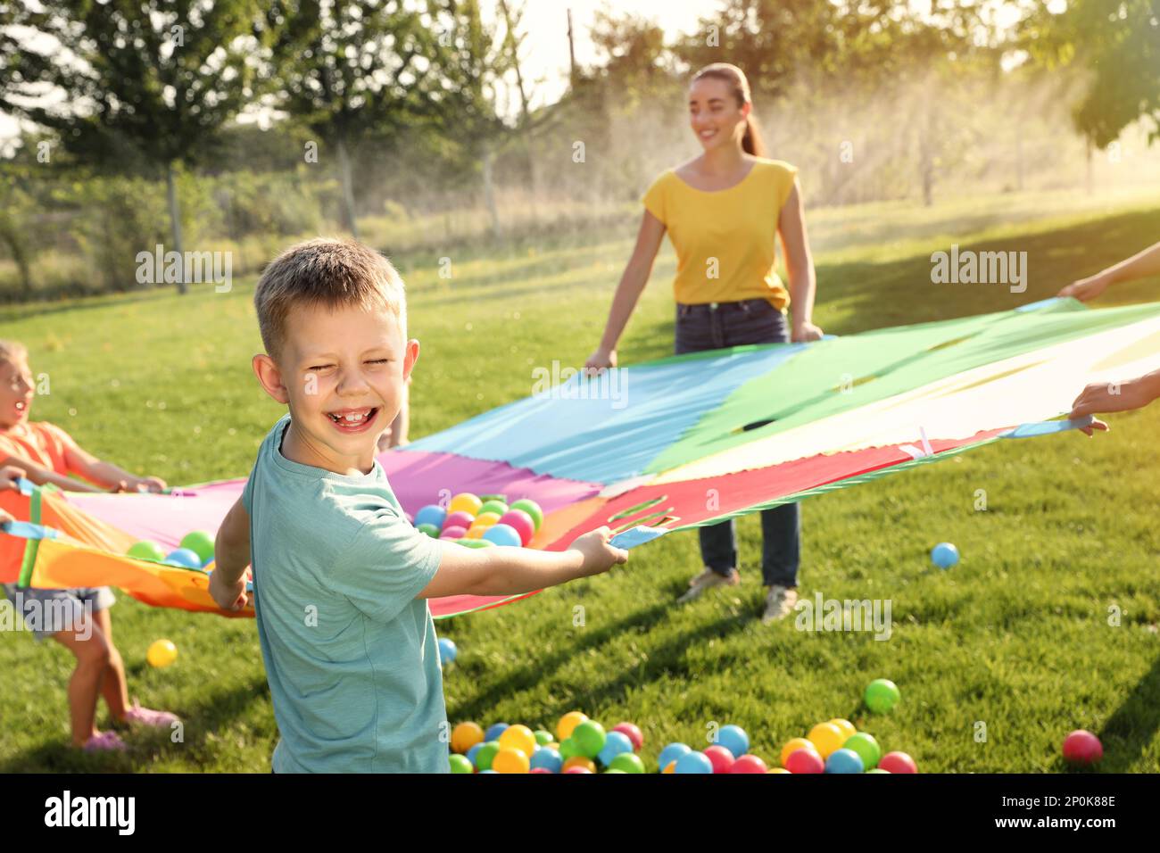 Group Of Children And Teacher Playing With Rainbow Playground Parachute 