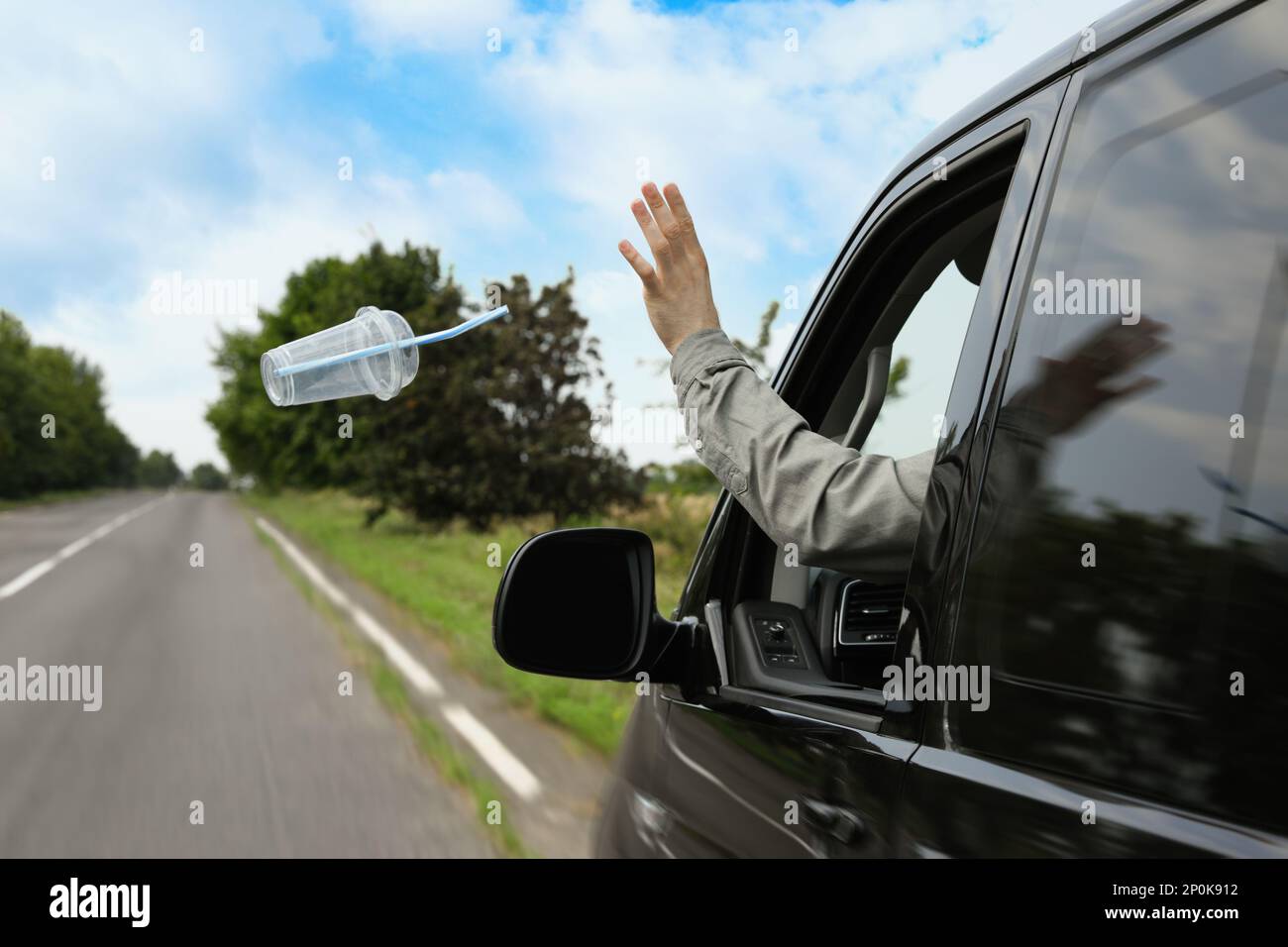 Driver throwing away plastic cup from car window. Garbage on road Stock