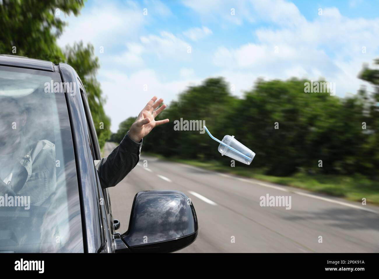 Driver throwing away plastic cup from car window. Garbage on road Stock