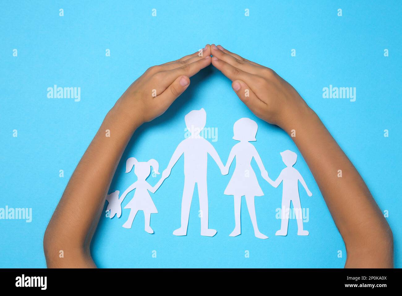 Child covering paper family figures with hands on light blue background ...