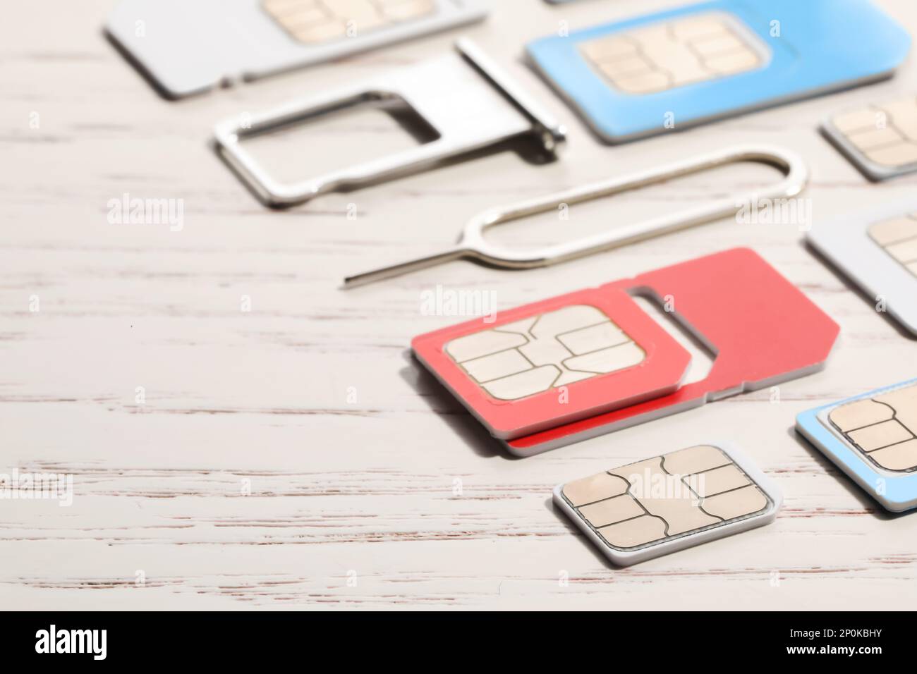 Different SIM cards, ejector and tray on white wooden background