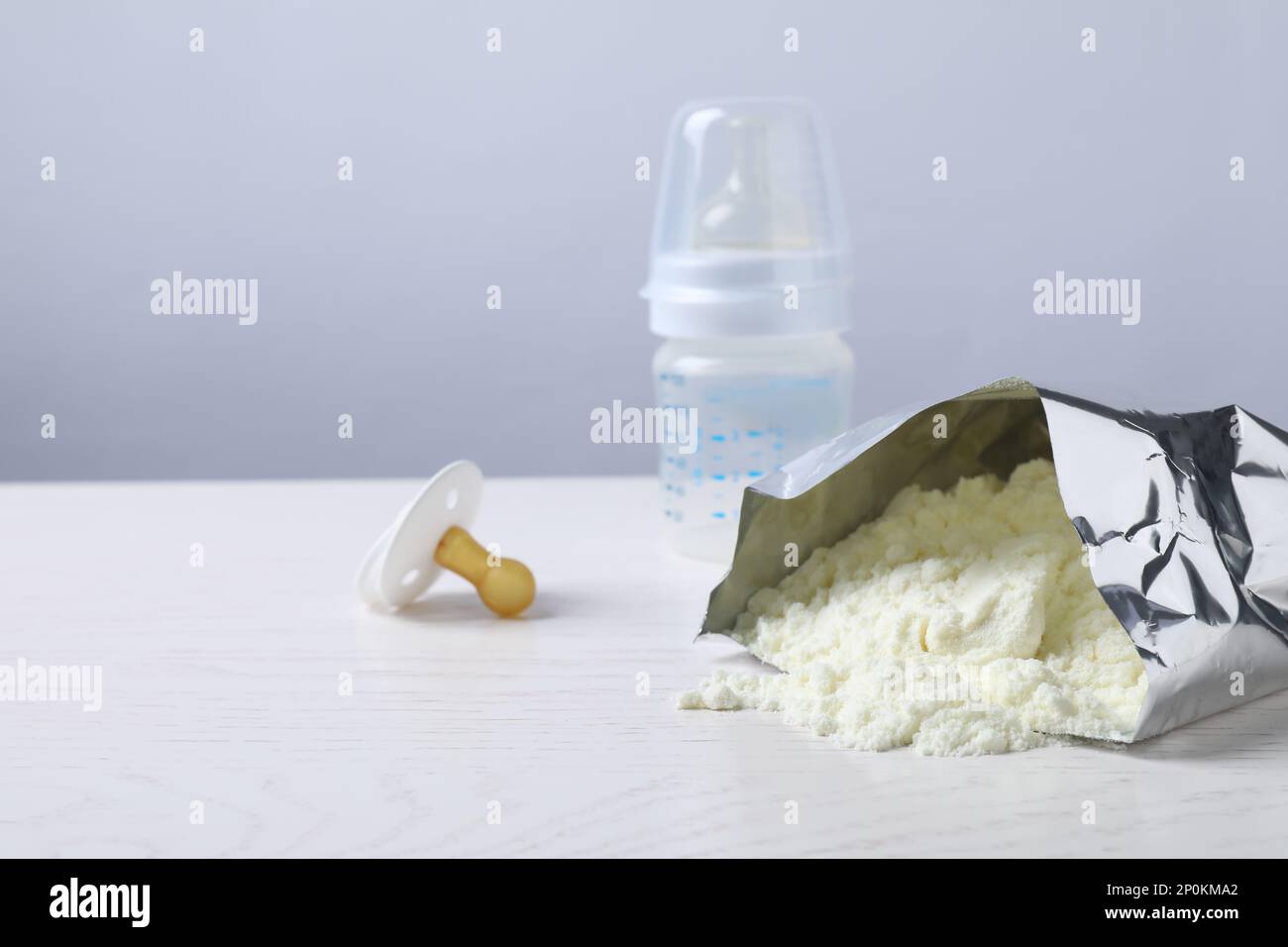 Bag of powdered infant formula, feeding bottle and pacifier on white