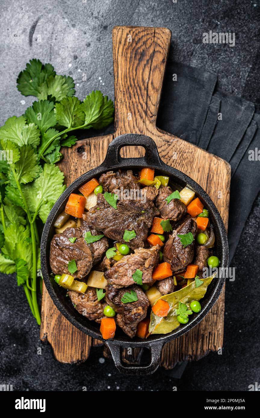 Beef stew with potato, carrot and herbs in a skillet. Black background