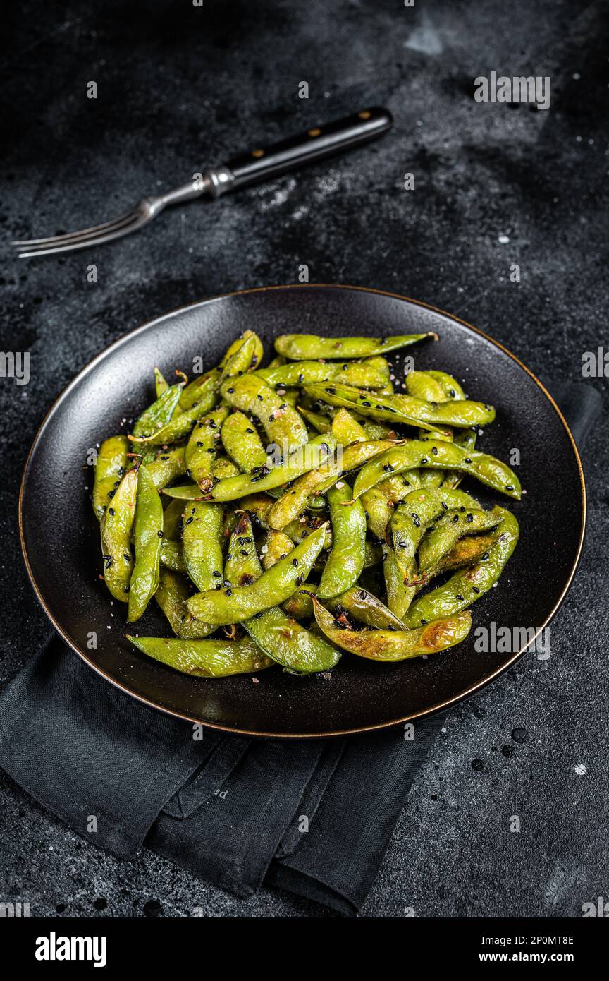 Stir-fried green Edamame Soy Beans with sea salt and sesame seeds in a plate. Black background. Top view. Stock Photo