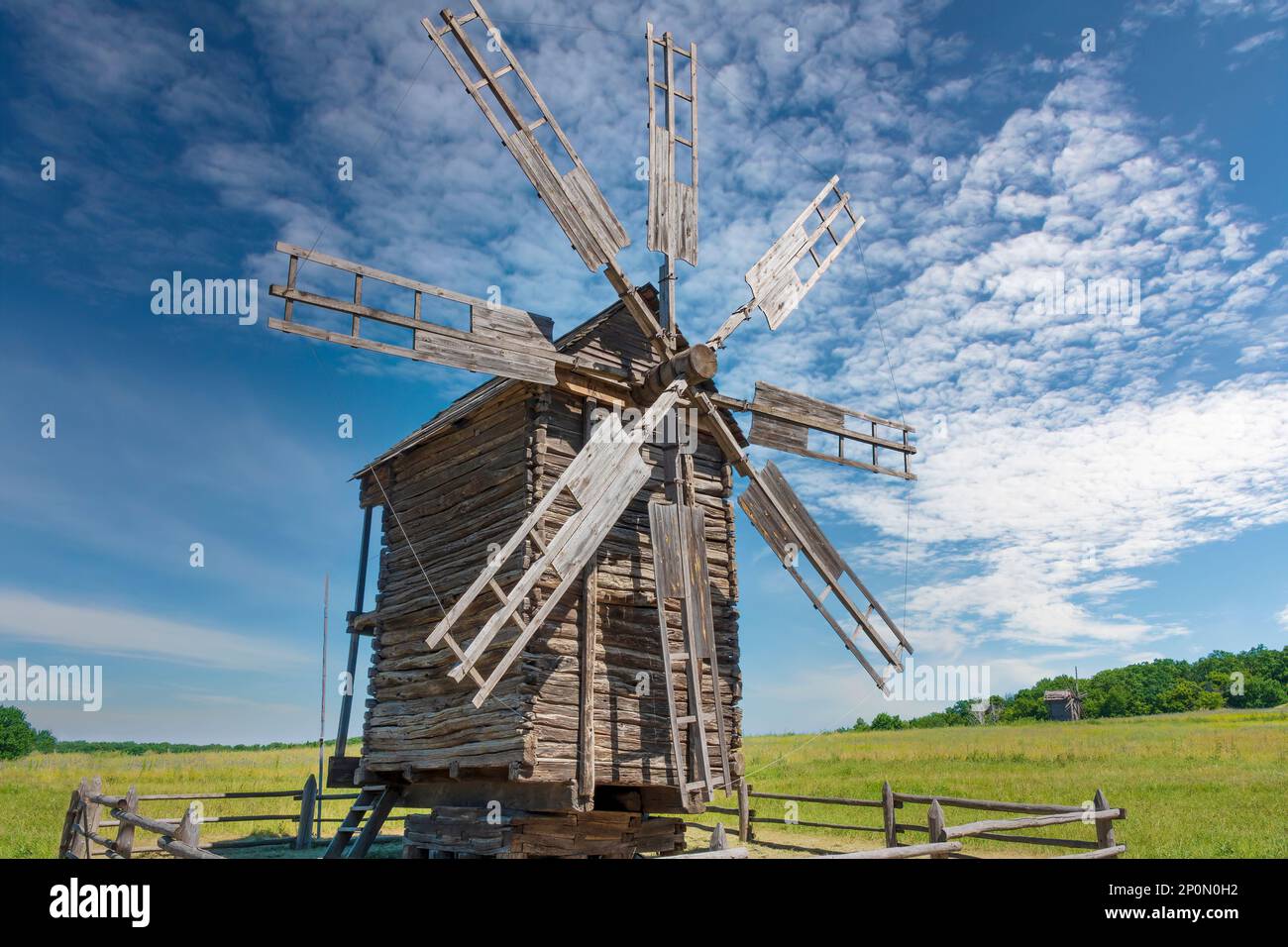 Old wooden windmill on the green meadow with scenic blue sky on the background. Stock Photo