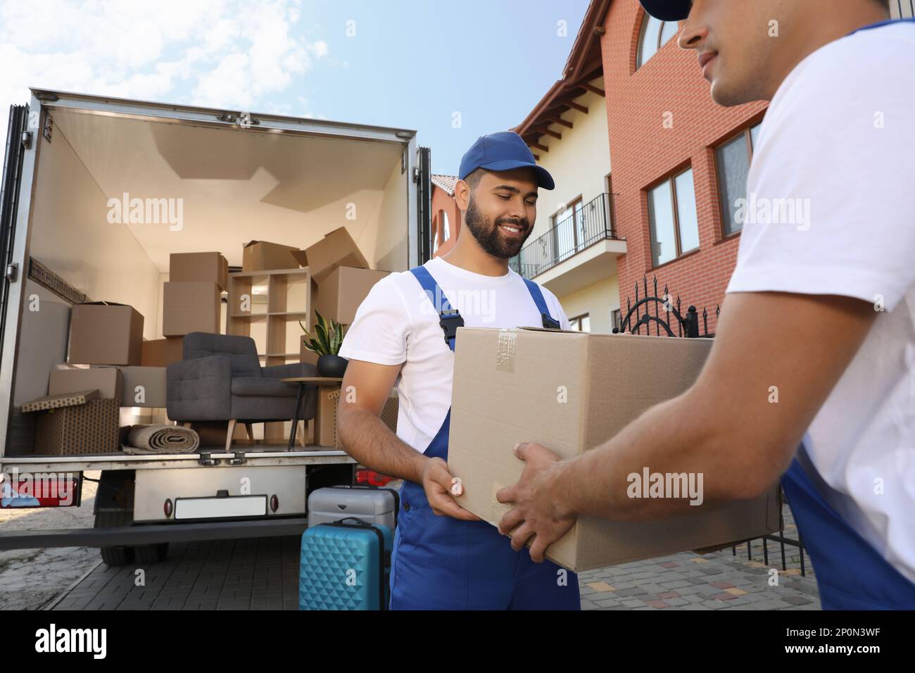 Workers unloading boxes from van outdoors. Moving service Stock Photo