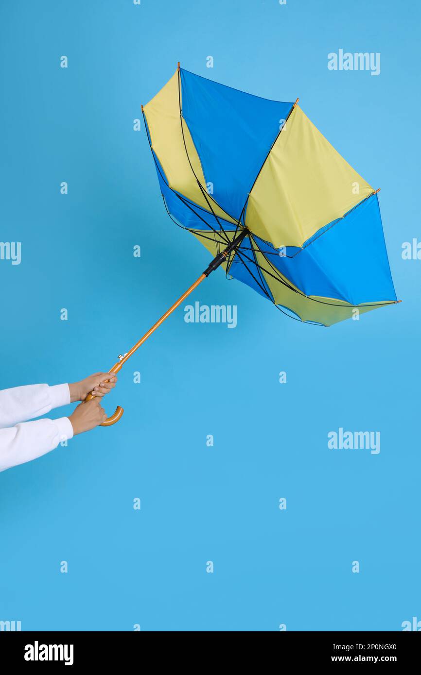 Woman with umbrella caught in gust of wind on light blue background, closeup Stock Photo