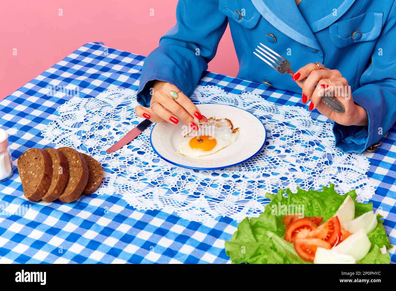 Top view image of female hand putting cigarette into egg yolk on fried eggs  at checkered retro tablecloth. Food pop art photography Stock Photo
