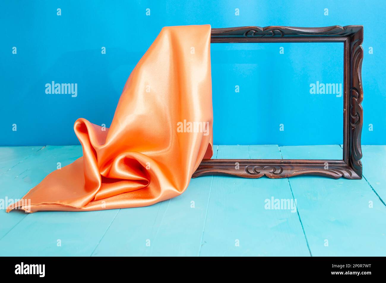 Empty wooden frame unveiled by an orange satin drape, on blue background Stock Photo