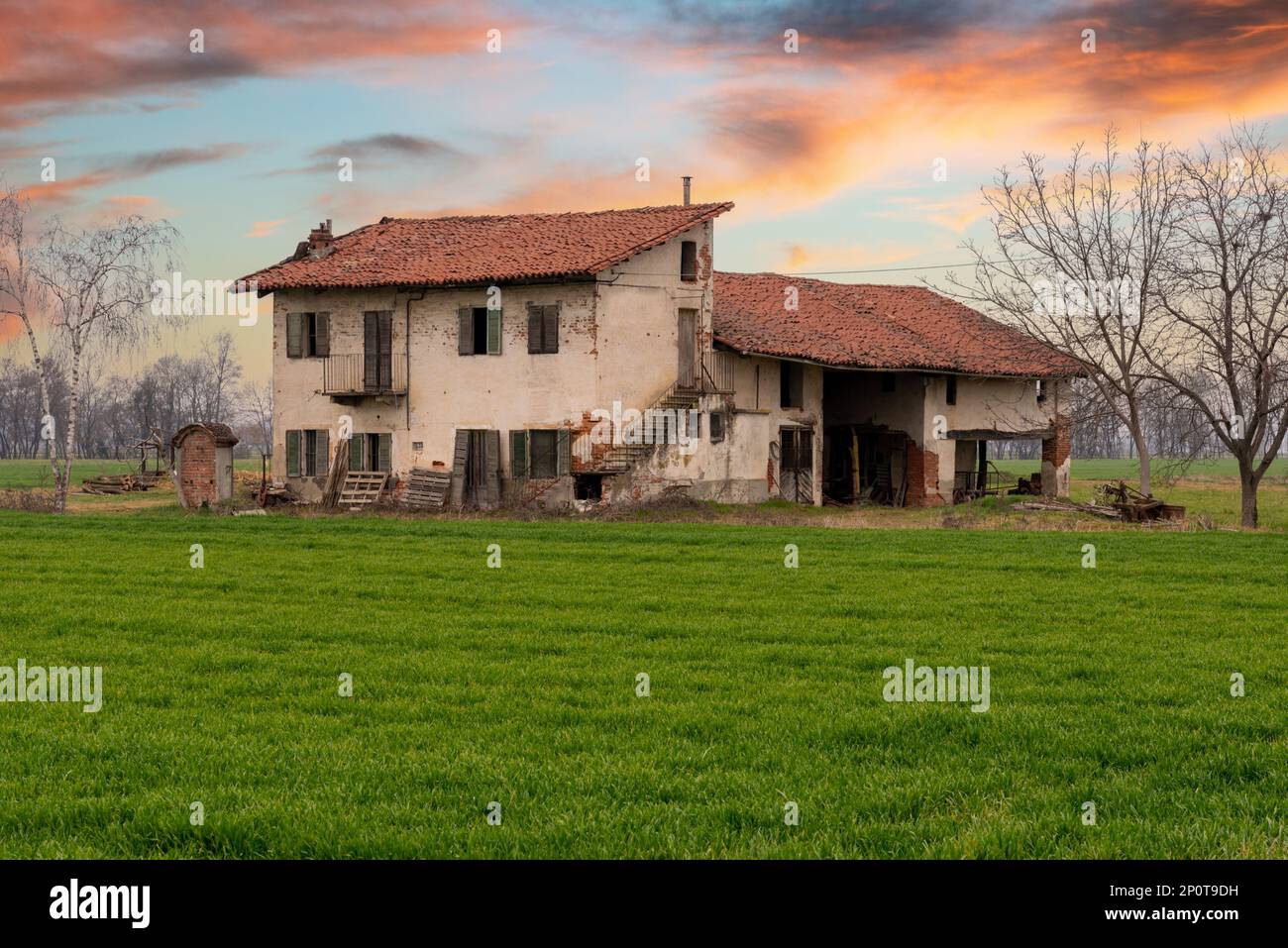Old abandoned italian farmhouse with typical rural architecture of the Po Valley in the province of Cuneo, Italy, at sunset with field of young green Stock Photo