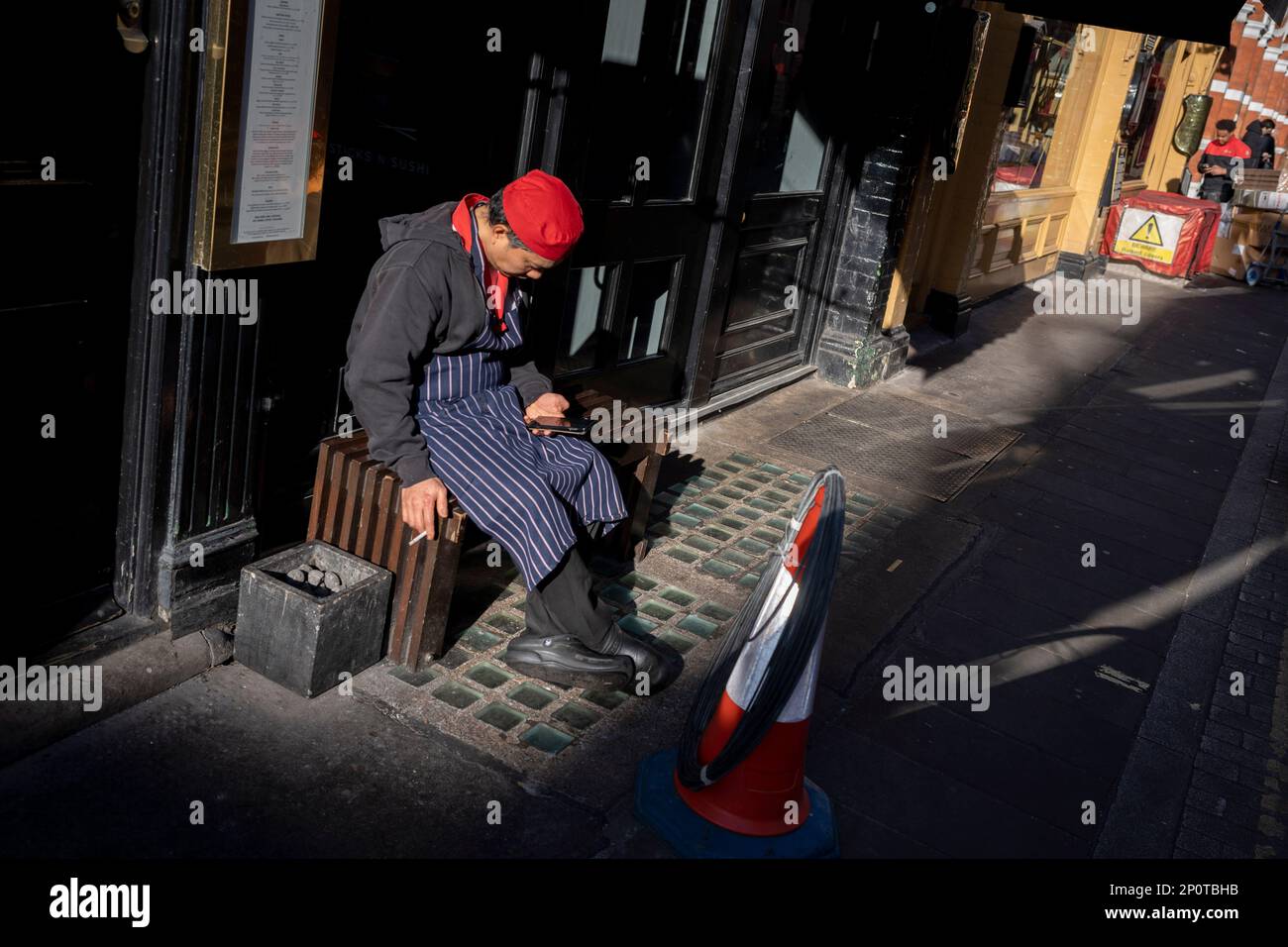 A chef takes a rest break and looks at his phone outside his place of work in the West End, on 2nd March 2023, in London, England. Stock Photo