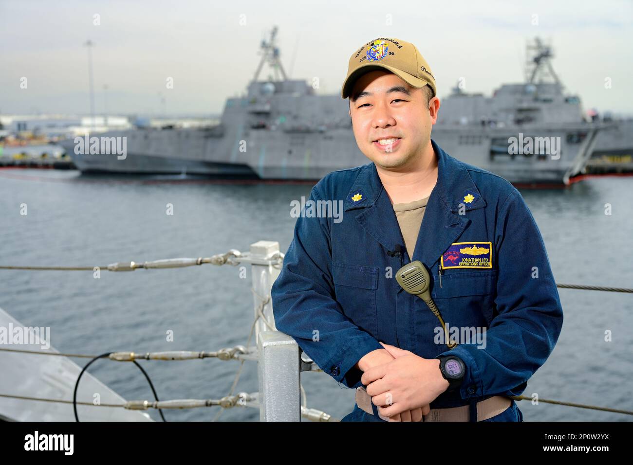 Lt. Cmdr. Jonathan Leo, operations officer of the Independence-class litorral combat ship USS Canberra (LCS 30), poses with the Independence-class LCS USS Kansas City (LCS 22) behind him in San Diego, Jan. 13, 2023, as Canberra prepares to participate in its Combat System Ship Qualification Trials. Leo also participated in the CSSQT of Kansas City during its pre-deployment qualification trials.     The CSSQT qualification process is a NAVSEA pre-deployment requirement to verify the crew’s ability to operate and maintain their combat systems in a safe and effective manner. It is considered a ma Stock Photo