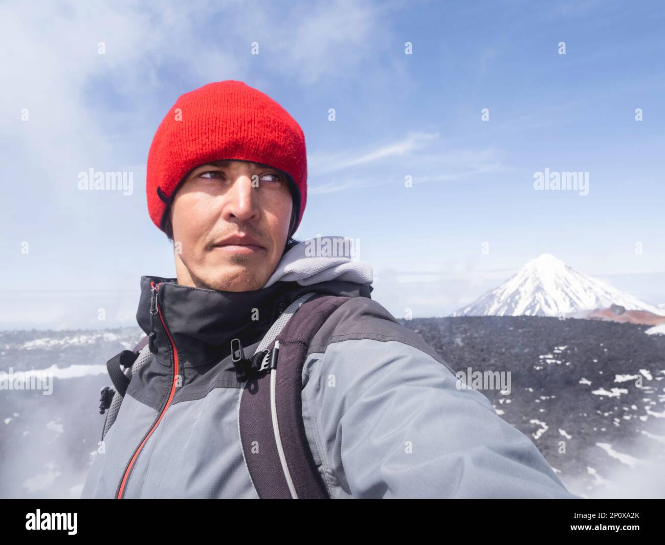 Tourist makes selfie on Avachinsky volcano. Koryaksky or Koryakskaya Sopka on background. Natural landmarks of Kamchatka Peninsula. Russia. Stock Photo