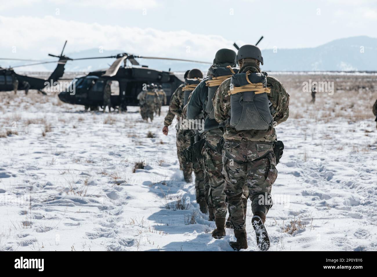 U.S. Army Paratroopers assigned to the 19th Special Forces Group (Airborne), Utah Army National Guard, walk single file to an awaiting UH-60 Black Hawk Helicopter from the 1-211th Aviation Battalion, for their static line jump on January 21, 2023 near Camp Williams, Utah. A static line jump is where a cord is attached at one end to the aircraft while the other end is attached to the top of the jumper's chute. When the parachutist falls from the aircraft it causes the static line to become tight and pulls the parachute out of the container on the jumper’s back. (Utah Army National Guard photo b Stock Photo