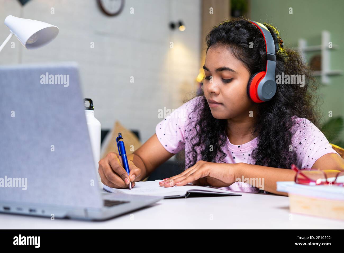Girl student making notes from online class using laptop at home by wearing wirless headphones - concept of development, learning and technology Stock Photo