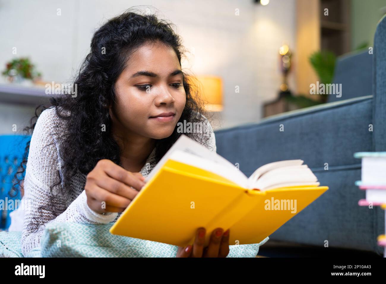 close up shot of girl reading book infront of sofa by laying on floor at home - concept of hobbies, wisdom and self development Stock Photo