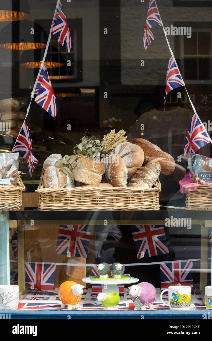Attractive window display in a bakery shop in Kirkby Stephen Cumbria with bread rolls, union jacks, herdwick models, baskets, mugs, wheat. Stock Photo