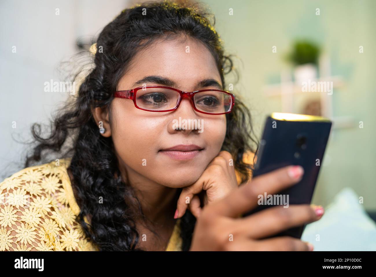 close up shot of young girl with eyeglasses using social media on mobile phone while sitting on sofa at home - concept of social media sharing Stock Photo