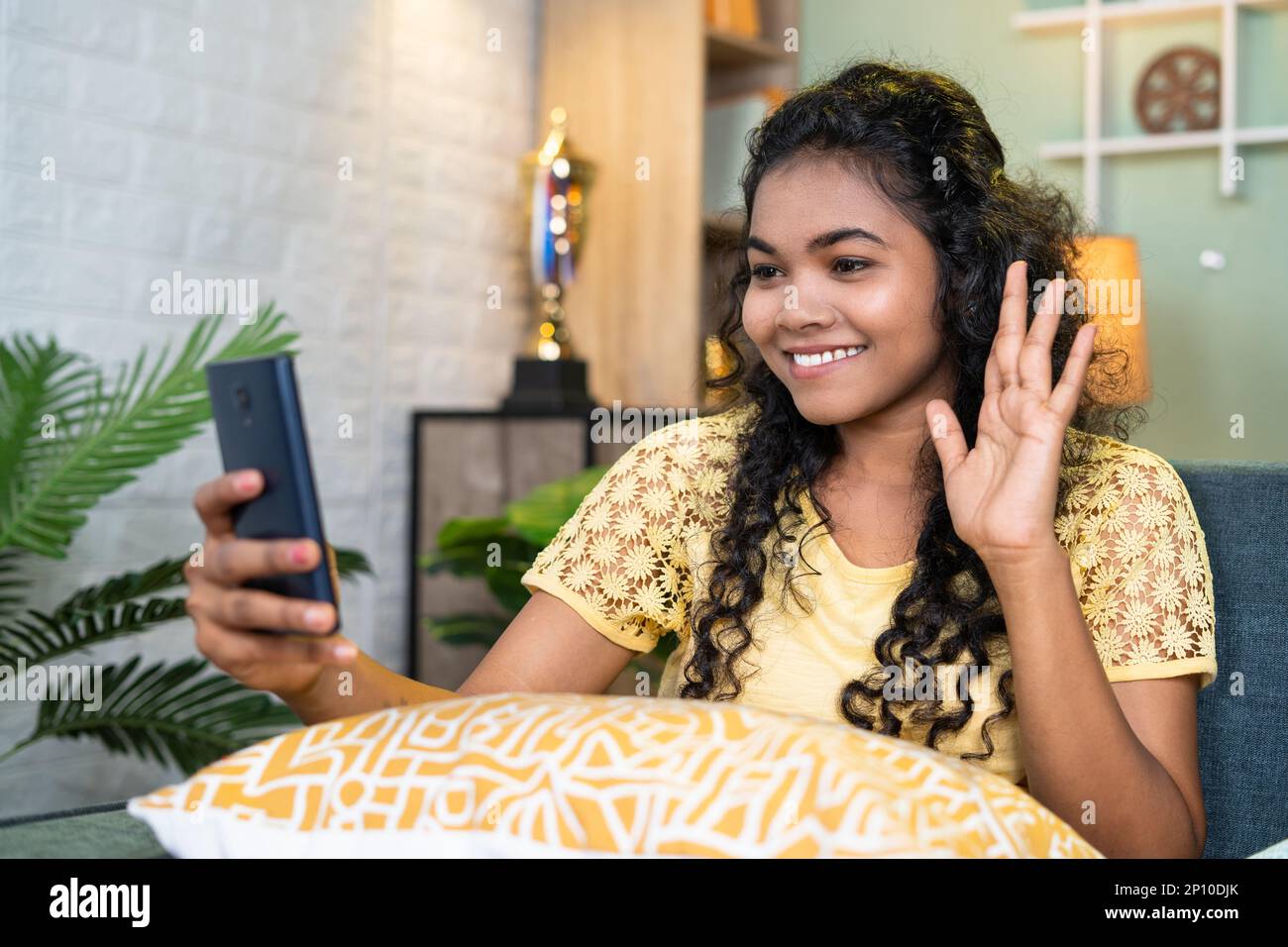 Happy young girl making talking with friends on video call from mobile phone at home -concept of technology, online chatting and happiness Stock Photo