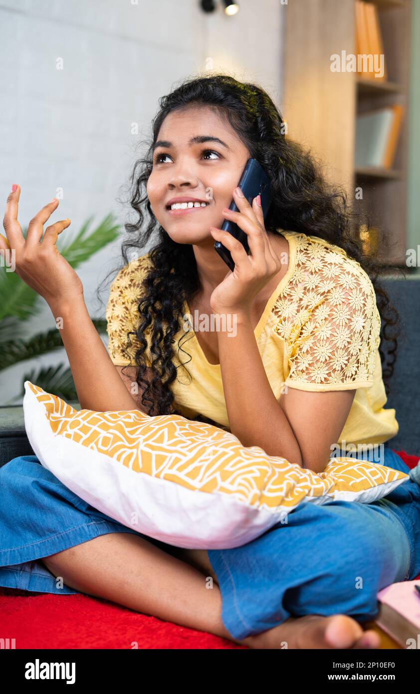 Smiling young teenager girl talking on mobile phone with friends while sitting on sofa at home - concept of communication, relaxation and technology Stock Photo