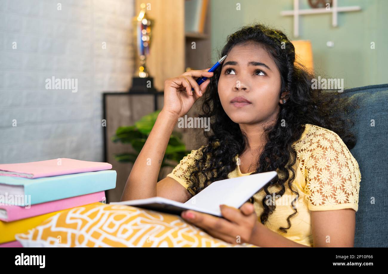 thoughful girl while reading book at home while sitting on sofa during exam preparation - concept of hard working, exam preparation and education Stock Photo